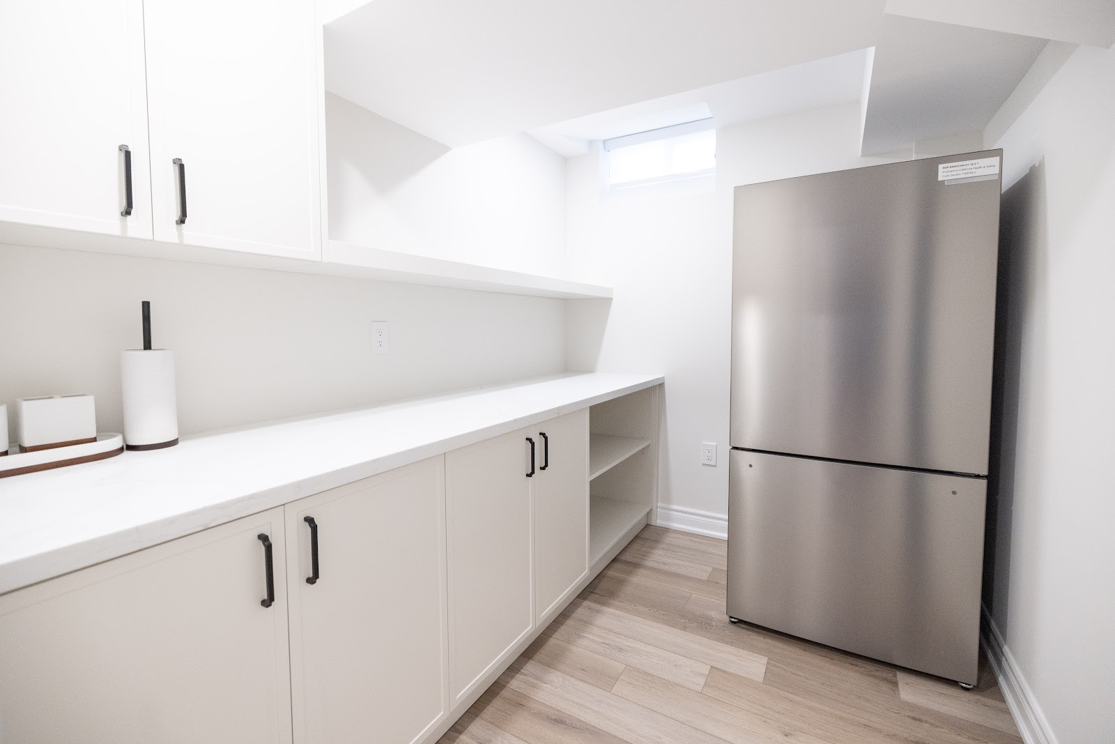 Basement kitchenette with white cabinetry and stainless bar fridge, Hamilton