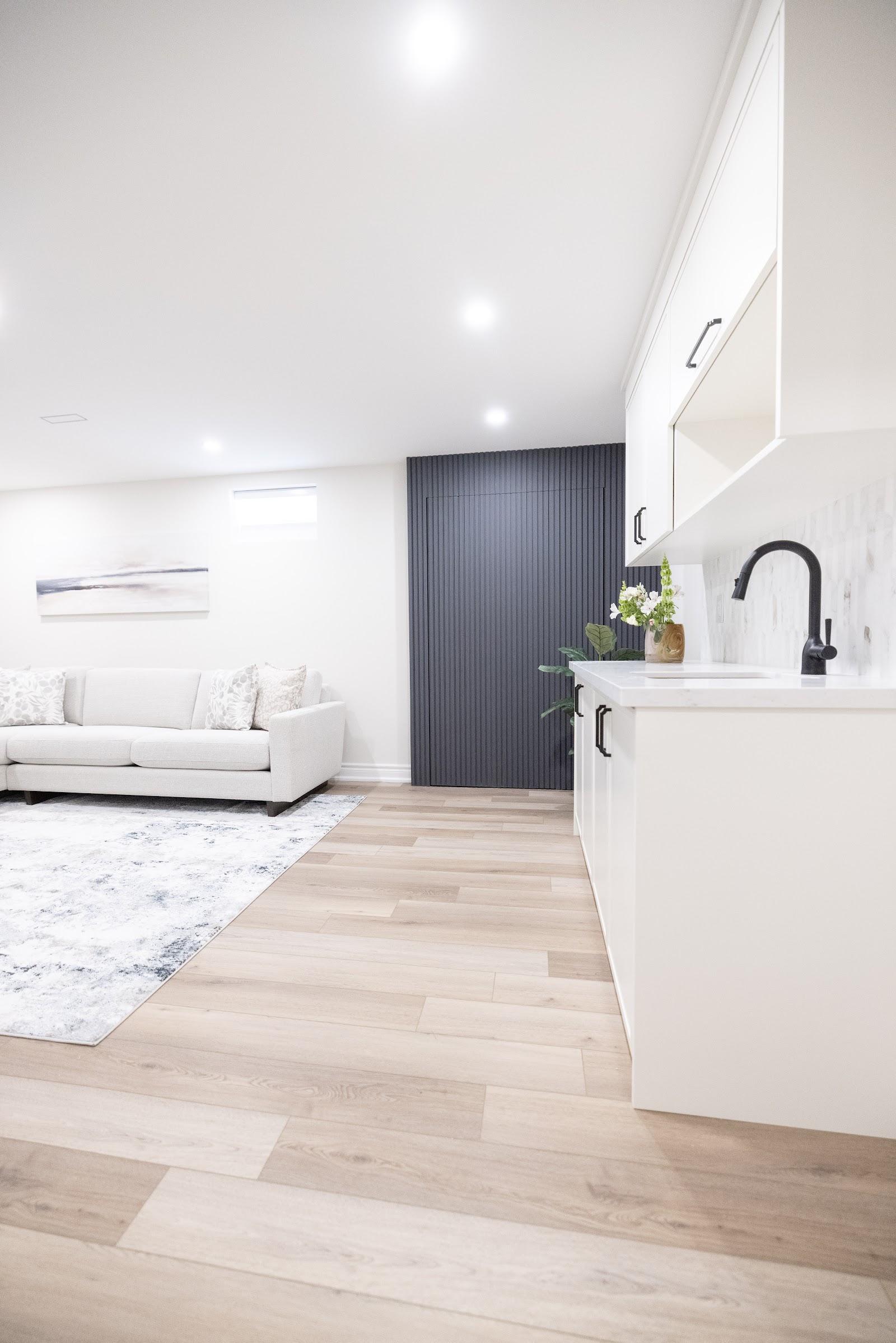 Basement wet bar with black gooseneck faucet and dark slat wall beside a lounge, Hamilton
