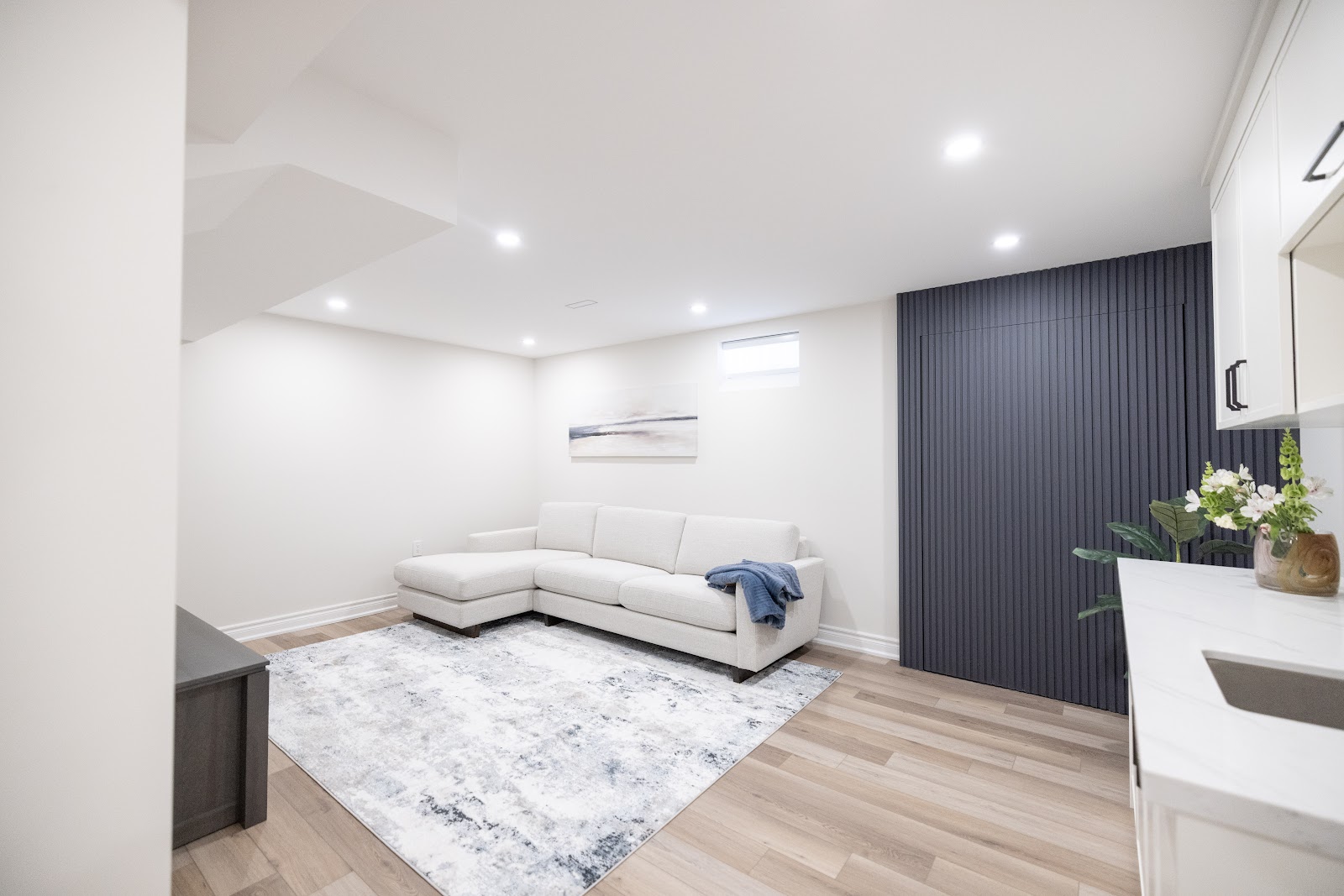 Finished basement lounge with white sectional sofa and dark slat feature wall, Hamilton renovation by Final Touch Contract